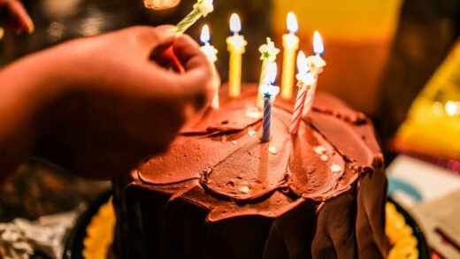 person holding lighted candle on brown cake